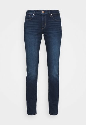 Jeans en denim bleu foncé, coupe slim, avec cinq poches, fermeture à bouton en métal, et surpiqûres contrastées près des poches. Texture lisse et design classique.