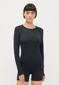 Svart långärmad träningsskjorta med ett strukturerat mönster, rund halsringning och åtsittande design. Kombinerad med svarta shorts.