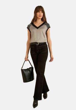 Graues und schwarzes V-Ausschnitt-Oberteil mit kurzen Ärmeln, kombiniert mit schwarzen ausgestellten Jeans und einer schwarzen Bucket-Bag, dazu spitze schwarze High Heels.