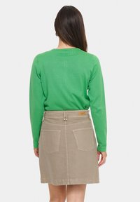 Maglia verde a maniche lunghe abbinata a una gonna di jeans beige. La gonna presenta due tasche posteriori e un'etichetta in pelle con il marchio sulla cintura.