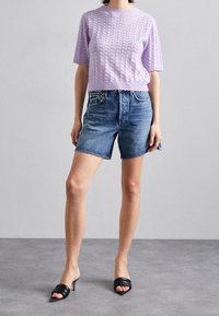 Lawendowy sweter na drutach z krótkimi rękawami, w połączeniu z niebieskimi szortami dżinsowymi. Czarny, na obcasie mule dopełniają stylizację. Prosty i codzienny design.