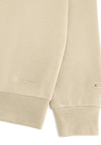 Sudadera beige con una textura suave, que presenta puños acanalados. Sutil logo bordado de "Champion" en la manga izquierda y en el pecho.