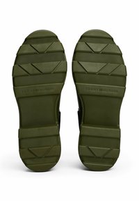 Donkergroene gestructureerde rubberen zolen van Tommy Hilfiger sandalen met geometrische looppatronen, naast elkaar weergegeven op een witte achtergrond.