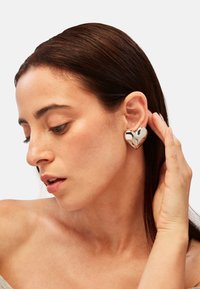 Stříbrné náušnice ve tvaru srdce s hladkým povrchem, se lesklým zpracováním. Nošeny na uchu, zvýrazňující jejich jedinečný design.