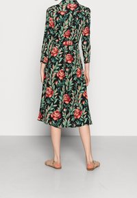 Abito floreale con sfondo nero, decorato con rose rosse e foglie verdi. Maniche lunghe e orlo al ginocchio con dettaglio di cintura annodata.