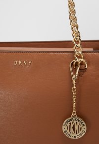 Bruine leren handtas met een geperst patroon, gouden DKNY-logo, gouden kettinghengsel en een ronde sleutelhanger met inscriptie "Donna Karan".