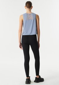 Lichtblauwe sporttanktop met een transparante mesh achterkant, gecombineerd met zwarte legging. De outfit heeft een relaxte pasvorm en is gemaakt van zachte, rekbare stof.