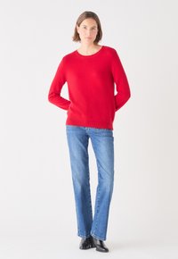 Maglione rosso lavorato a maglia con collo rotondo, maniche lunghe, abbinato a jeans a gamba dritta di un blu chiaro e stivali alla caviglia neri. Texture liscia.