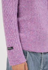 Violetti neulottu villapaita, jossa on tekstuuri-kuvio, resorit hihansuissa ja helmassa. Hihassa pieni musta "BDG"-merkkinen lappu.