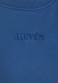 Blaues Baumwoll-T-Shirt mit geripptem Rundhalsausschnitt, das ein erhabenes, tonal gesticktes "Levi's"-Logo auf der Vorderseite aufweist. Glatte Textur, keine weiteren Muster.