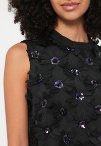 Μαύρο τοπ με υφασμάτινες εφαρμογές λουλουδιών· διαθέτει ιριδίζουσες πούλιες στο κέντρο των λουλουδιών· αμάνικο σχέδιο· υφασμένο επιφάνεια.