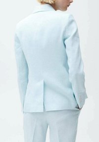 Costume en lin bleu clair avec une coupe ajustée, doté d'une fente unique et de manches longues. Texture lisse avec un léger éclat, pantalon assorti.