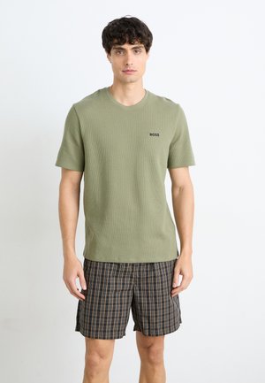 T-shirt texturé vert olive à manches courtes avec un col ras du cou et un logo noir ; associé à un short à carreaux sombre avec des accents marron.