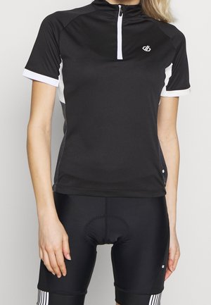 Vrouw draagt een zwart fietsjersey met korte mouwen met witte rits en zwarte gewatteerde fietsshorts met witte streepdetails.