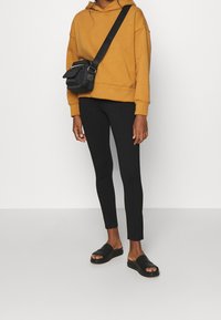 Senapsgul huvtröja, svarta leggings och svarta slidessandaler. Inkluderar en liten svart axelväska. Enkel och funktionell design.