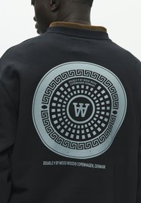 Sweat-shirt noir avec un motif circulaire bleu à motif quadrillé et un logo "W" au dos. Détail col marron. Tissu résistant.