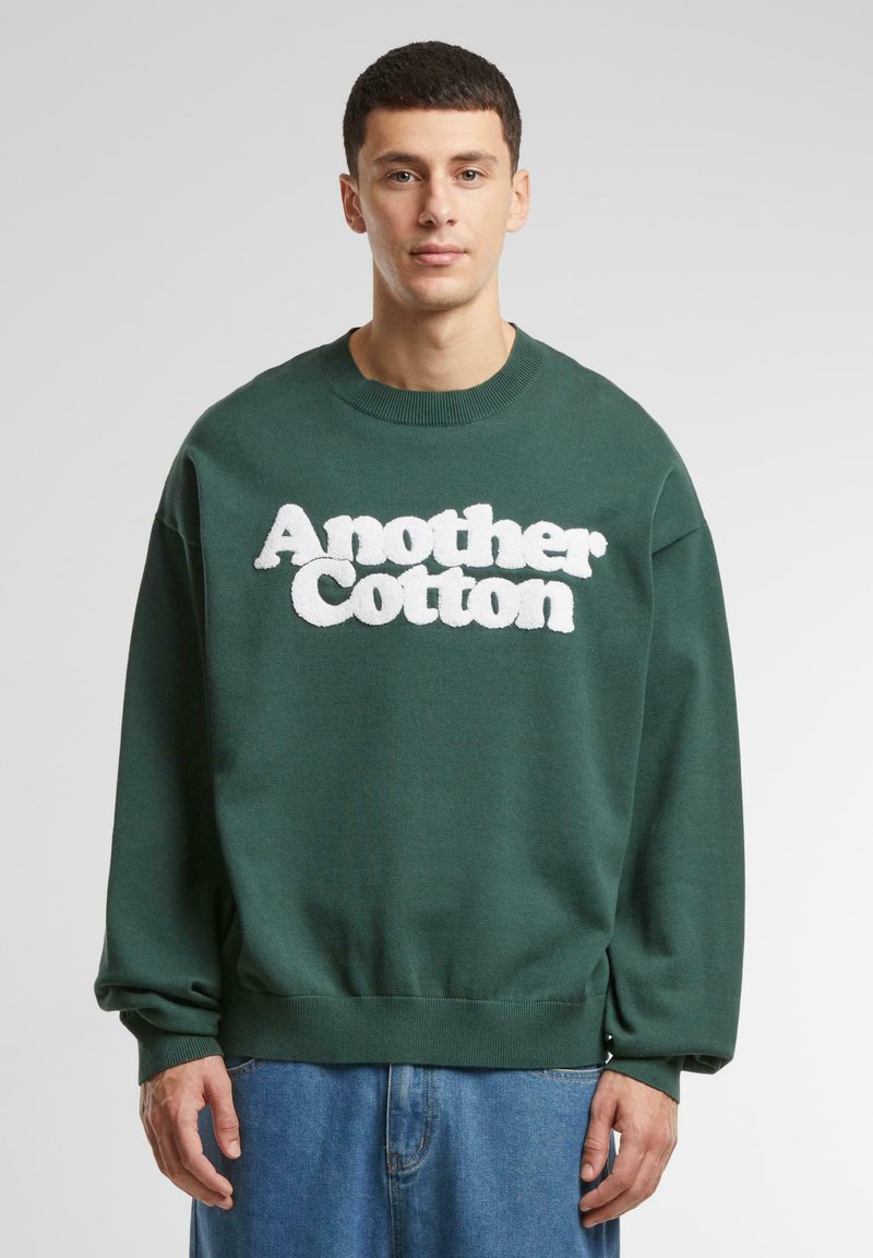 Sudadera de algodón verde con lettering esponjoso blanco "Another Cotton", cuello redondo y corte holgado con mangas acampanadas.
