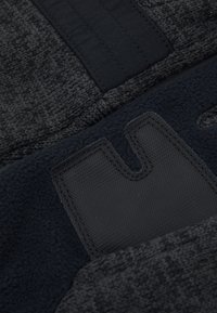 Tejido textil negro con un punto texturizado, una banda elástica suave y un parche de goma negra con un diseño troquelado.