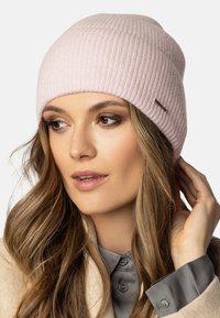 Bonnet en tricot à côtes rose avec un dessus arrondi et une étiquette de marque subtile sur le côté, fabriqué en matériau doux, s'adapte parfaitement à la tête.