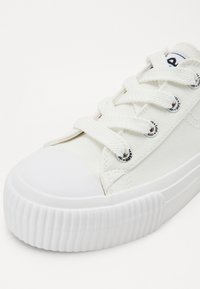 Baskets en toile blanches avec une finition texturée, un bout rond et des lacets plats. Comprennent des œillets marqués et une semelle en caoutchouc nervurée.