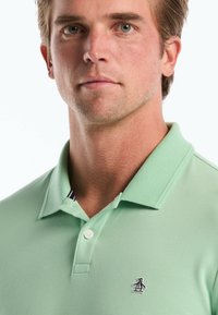 Lichtgroen poloshirt van een geweven stof, met twee knopen en een pinguïnlogo op de linkerkant van de borst. Voorzien van een contrasterende kraag.