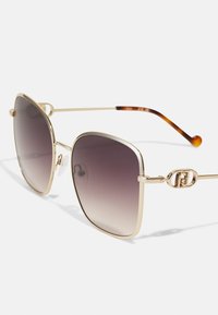 Gafas de sol de metal dorado con grandes lentes cuadrados, que van de un púrpura oscuro a un tono claro. El diseño minimalista presenta acentos de logo y puntas de patilla de carey.