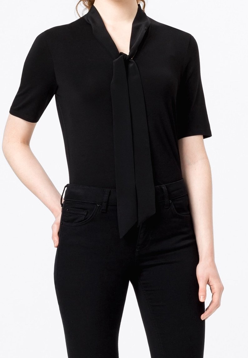 Musta, lyhythihainen paita, jossa on solmittava kaulustus, valmistettu sileästä kankaasta. Yhdistetty mustiin istuviin farkkuihin, luoden moniokromaattisen asun.