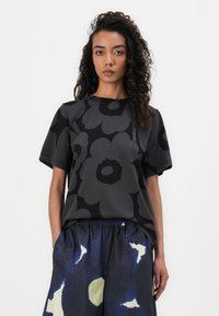 Black short-sleeve top with a large flower pattern, paired with loose blue trousers featuring abstract white and yellow shapes.
