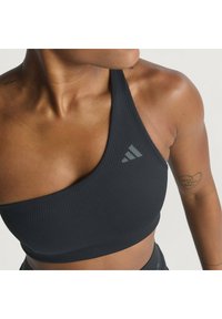 Sostegno sportivo nero a costine con un design a spalla unica. Presenta un tessuto testurizzato e un piccolo logo grigio sul lato sinistro superiore.