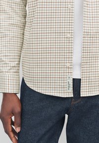 White checkered shirt with brown grid lines and button front, paired with dark denim jeans. Features a tag labeled "Durable Goods."