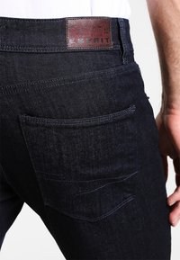 Pantalones vaqueros de mezclilla oscura con un diseño ajustado, que cuentan con una etiqueta de cuero marrón con la marca "ESPRIT" y un bolsillo trasero con un detalle de costura curva.