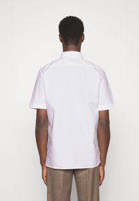Camisa blanca de manga corta con cuello, hecha de tela suave. Presenta un dobladillo recto y aberturas laterales para mayor libertad de movimiento.