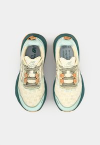 Chaussures de randonnée légères en crème et teal. Elles présentent une tige en mesh respirant, une semelle en caoutchouc texturée et des accents orange sur les lacets.