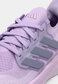 Chaussure de sport violette avec tige en maille texturée, lacets plats et trois rayures grises. Design léger avec un col rembourré pour le confort.