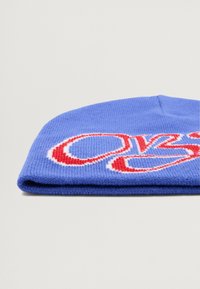 Gorro de punto azul con dobladillo, que presenta letras bordadas en rojo y blanco. El material es suave y con textura acanalada.