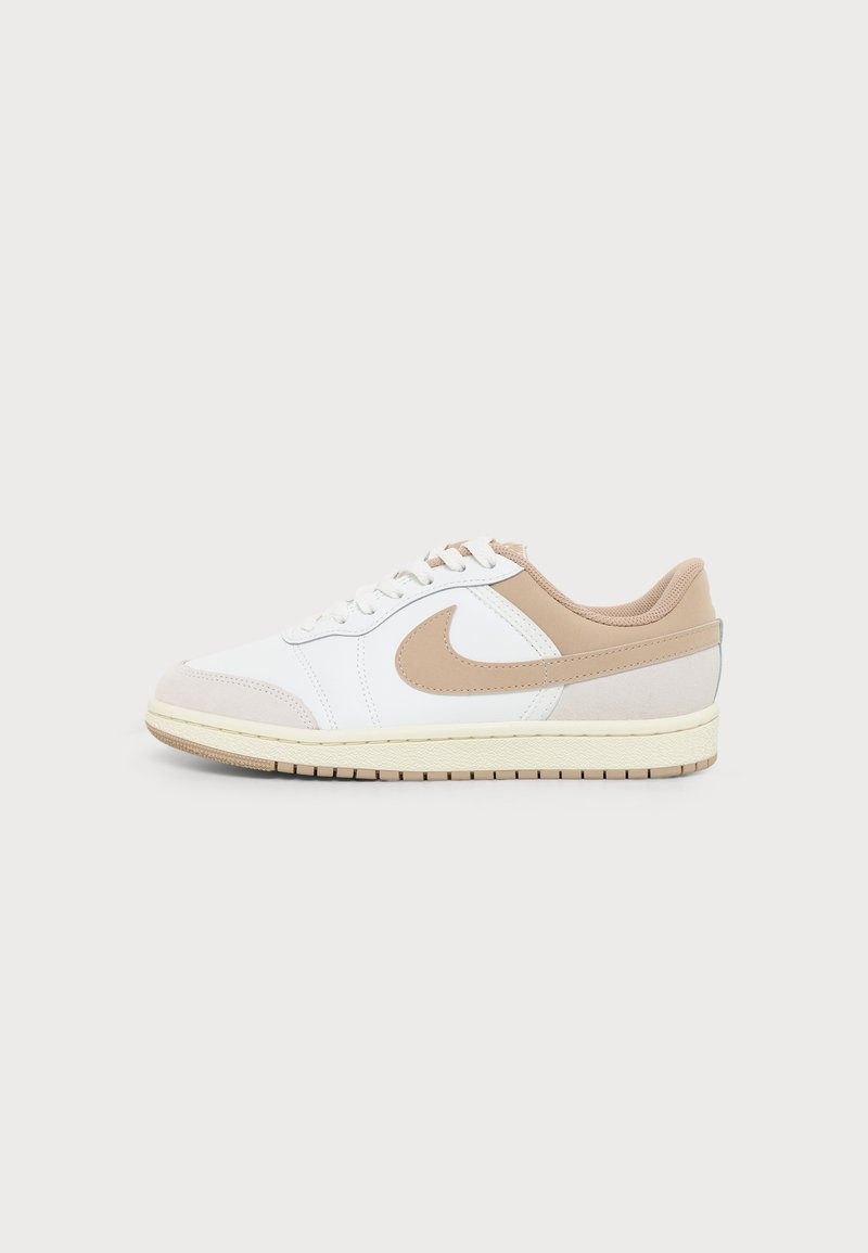 Baskets basses en cuir blanc avec des accents beiges, un swoosh Nike beige, un talon beige, des lacets blancs et une semelle en caoutchouc beige.