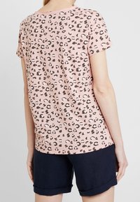 Camiseta rosa de manga corta con un estampado de leopardo negro. Tejido suave, corte relajado, combinada con pantalones cortos azul marino con dobladillo enrollado.