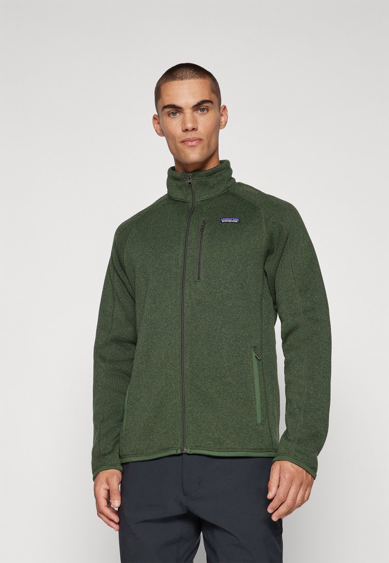 Dark green fleece jacket with high collar, full zip front, side pockets, ribbed cuffs, and a small logo on the chest. Soft texture overall.