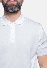 Polo shirt bianco a maniche corte con colletto classico e patta con tre bottoni, caratterizzato da una texture morbida e leggera.