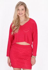 Röd stickad tvådelad outfit bestående av en kortärmad topp och en matchande högmidjad kjol, båda med ett texturerat mönster.