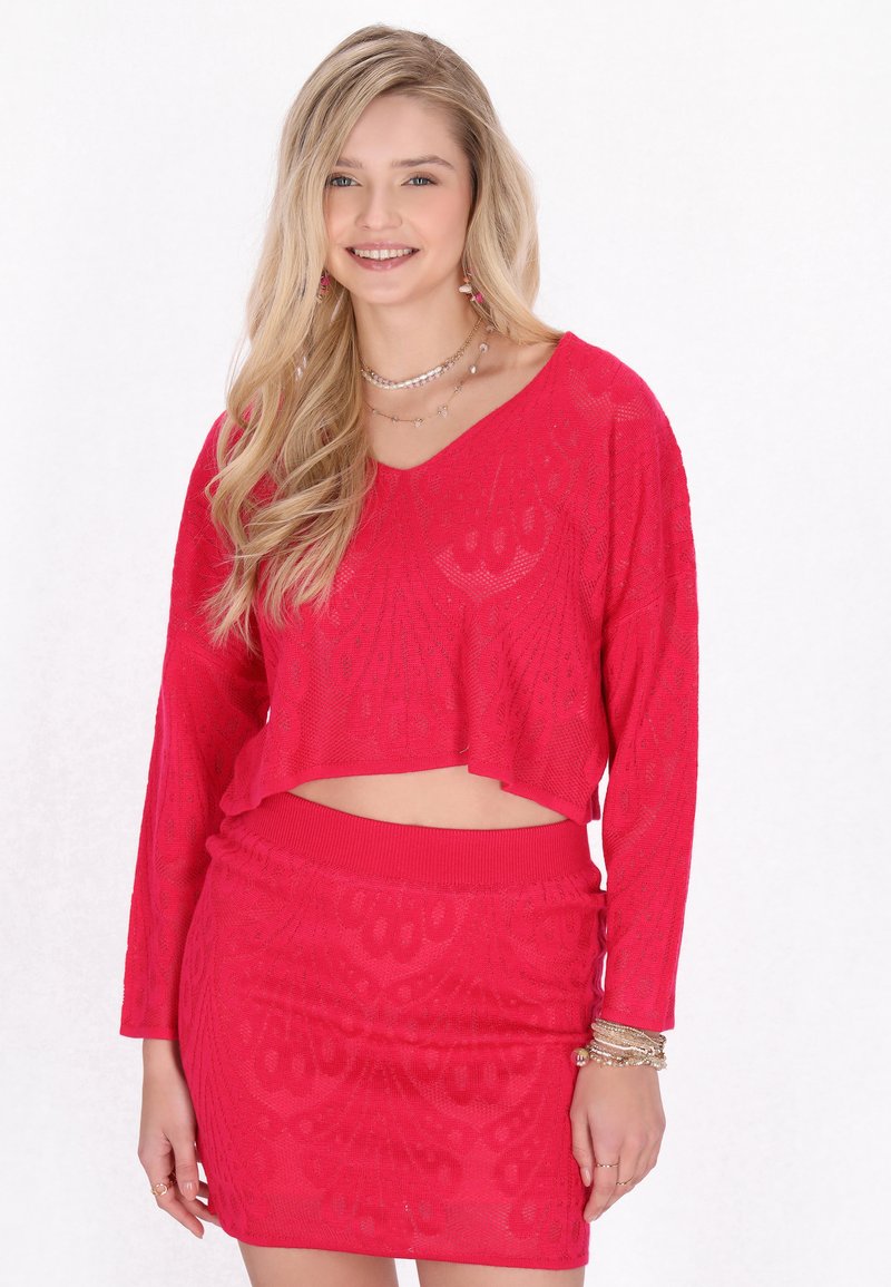 Röd stickad tvådelad outfit bestående av en kortärmad topp och en matchande högmidjad kjol, båda med ett texturerat mönster.