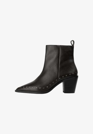 Botas de tobillo de cuero negro con punta afilada, tacón de bloque y tachuelas metálicas a lo largo del borde exterior. Cuenta con una tira en la parte posterior para facilitar su puesta.