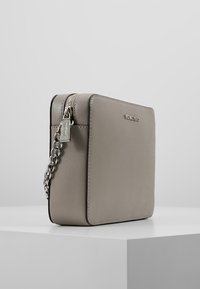 Bolso cruzado de piel sintética gris con forma rectangular, asa de cadena plateada, cierre de cremallera y un logotipo de la marca minimalista en la parte frontal.