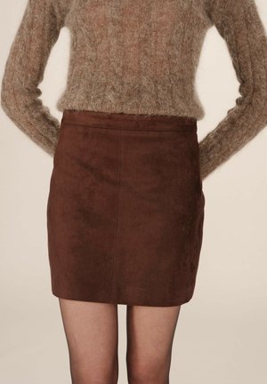 Mini jupe en daim marron avec une texture lisse, présentant un design ajusté et des coutures discrètes. Associée à un pull beige en peluche.