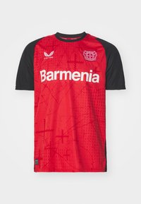 Camisola de futebol vermelha com mangas pretas, apresenta o logótipo da 'Barmenia' e o emblema do clube. O padrão texturizado no tecido adiciona interesse visual.