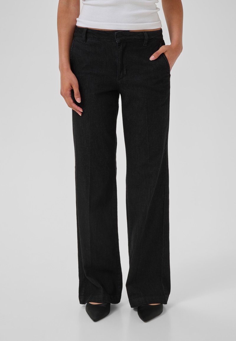 Pantalon noir à jambes larges en denim, avec une poche avant et une braguette zippée. Texture lisse avec des détails de couture subtils.