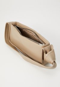 Beżowa skórzana torba na ramię o gładkiej fakturze, prostokątnym kształcie i zapięciem na zamek. Posiada szczegół zawiązanej paski. Wewnątrz podszyta.