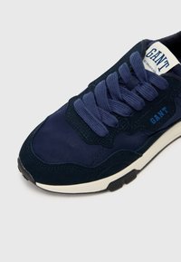 Navy blue sneaker with a combination of smooth and textured materials, featuring thick laces, a round toe, and "GANT" branding on the tongue.