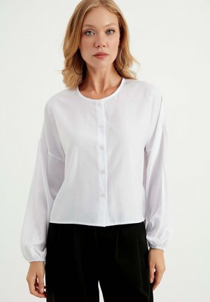 Camicia bianca con bottoni, realizzata in tessuto leggero, con scollatura rotonda, maniche lunghe, polsini elasticizzati e un design accorciato.