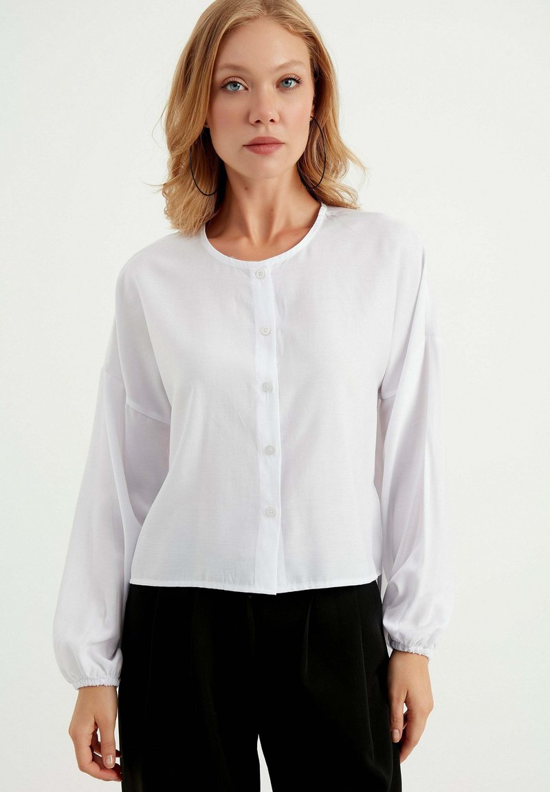Hvid skjorte med knapper lavet af letvægtsstof, med rund halsudskæring, lange ærmer, elastiske manchetter og et cropped design.
